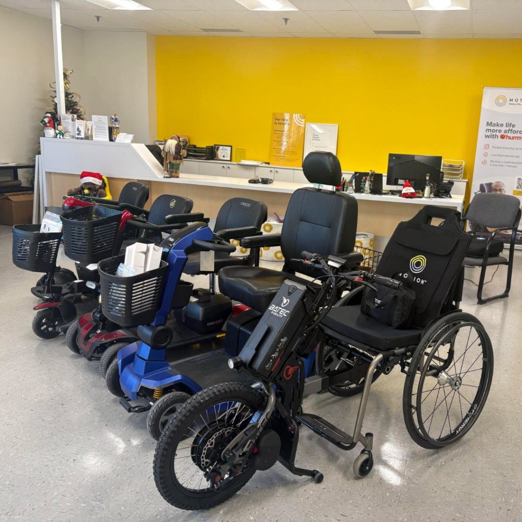 Line up of mobility devices in a Motion showroom with a yellow care desk wall in the background