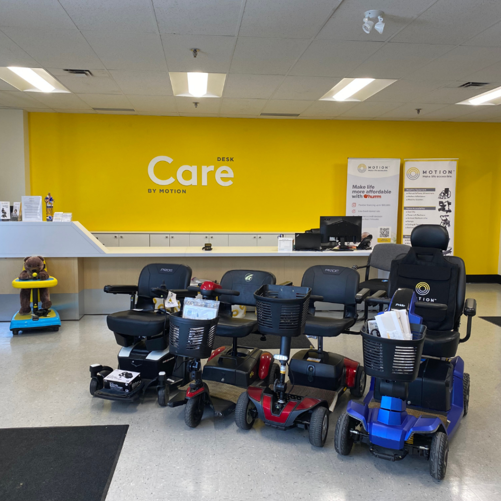 Interior view of the Motion Winnipeg Showroom, including a line up of power wheelchairs and mobility scooters with a yellow care desk wall in the background