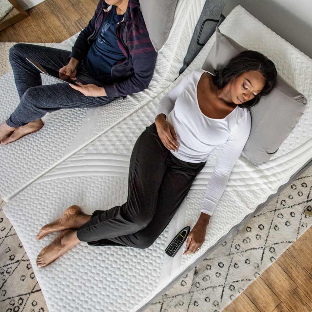 Woman and a man laying on a bed on separate mattresses.