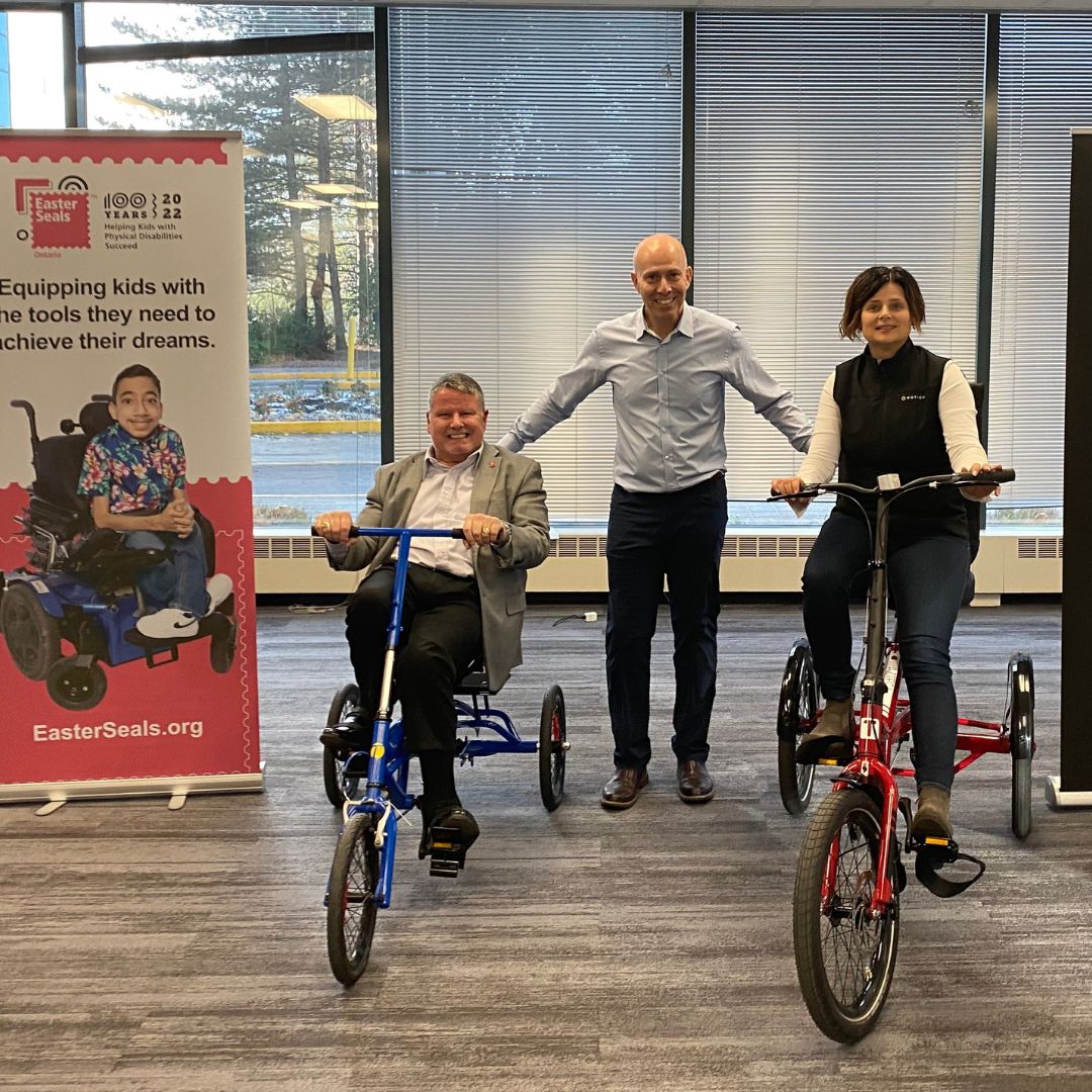 Motion CEO Sue Gilpin on adaptive bicycle with Easter Seals Ontario President and CEO Kevin Collins on adaptive bicycle and Jeff Fishbein in centre from Trivel bikes