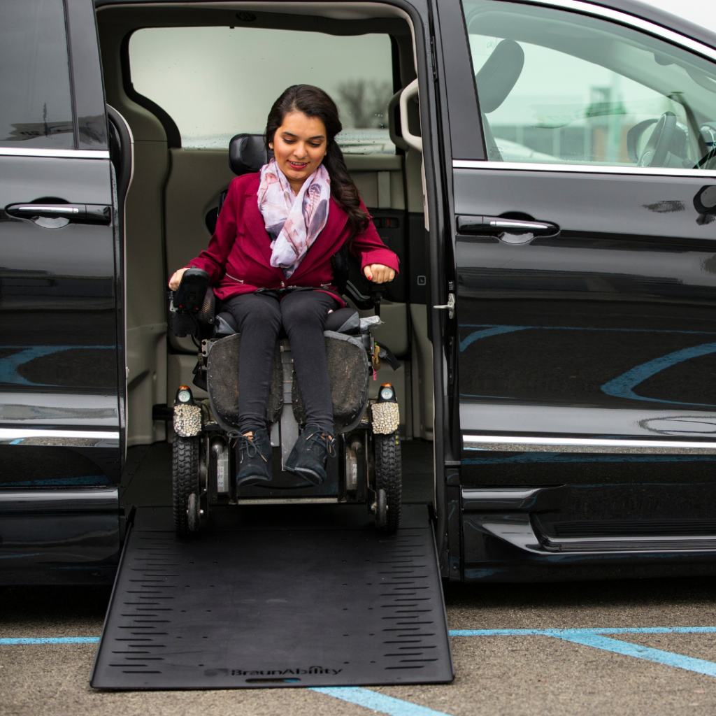 Young woman using power wheelchair to exit out of accessible vehicle with ramp at side entry