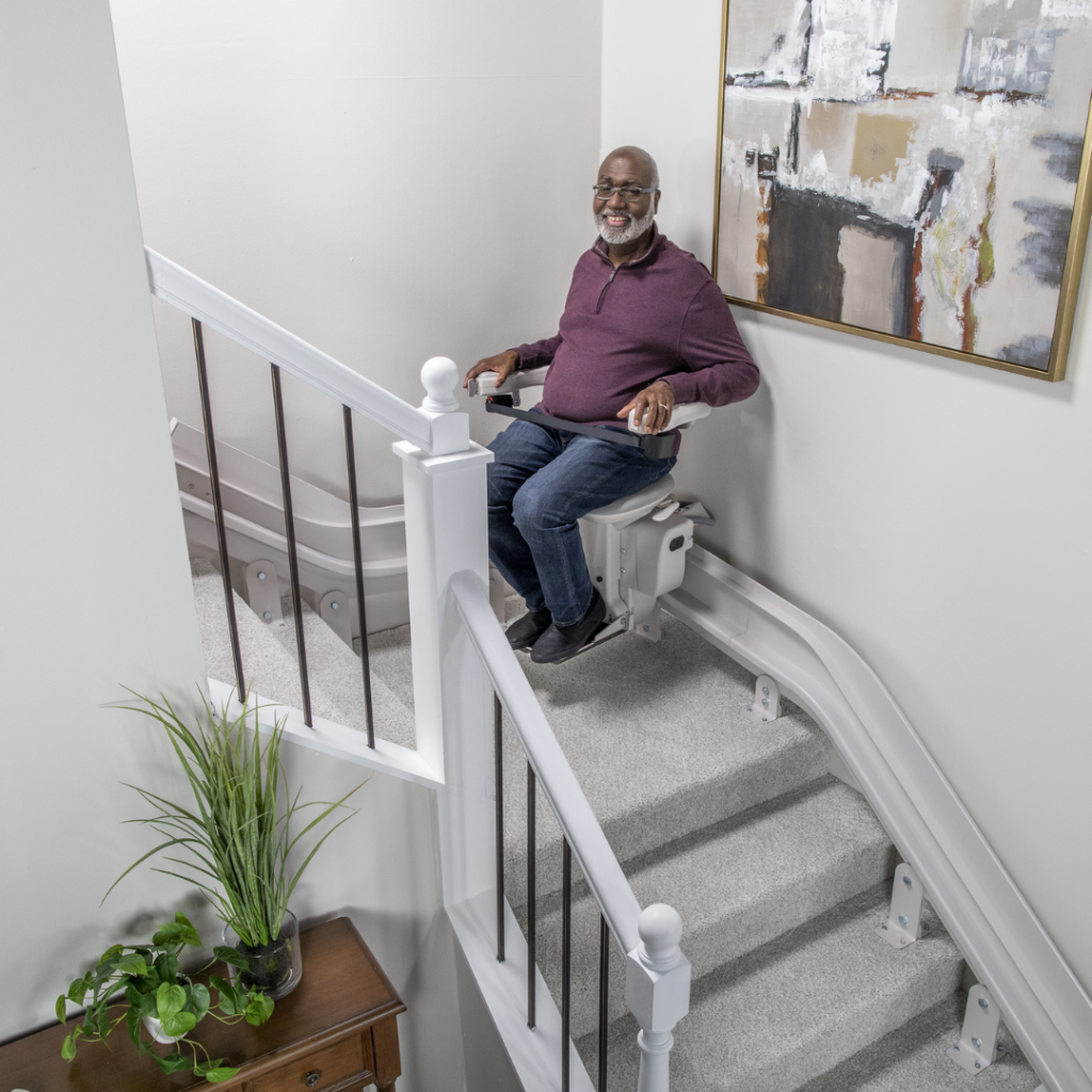 Senior man seated on a stairlift that is traveling up a curved staircase.