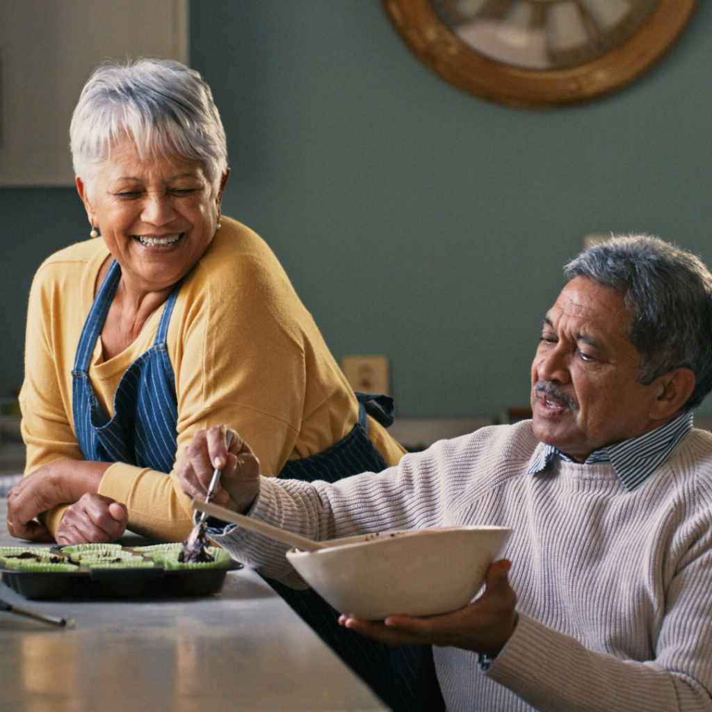 Man seated in wheelchair prepping meal with smiling woman leaning on counter looking on