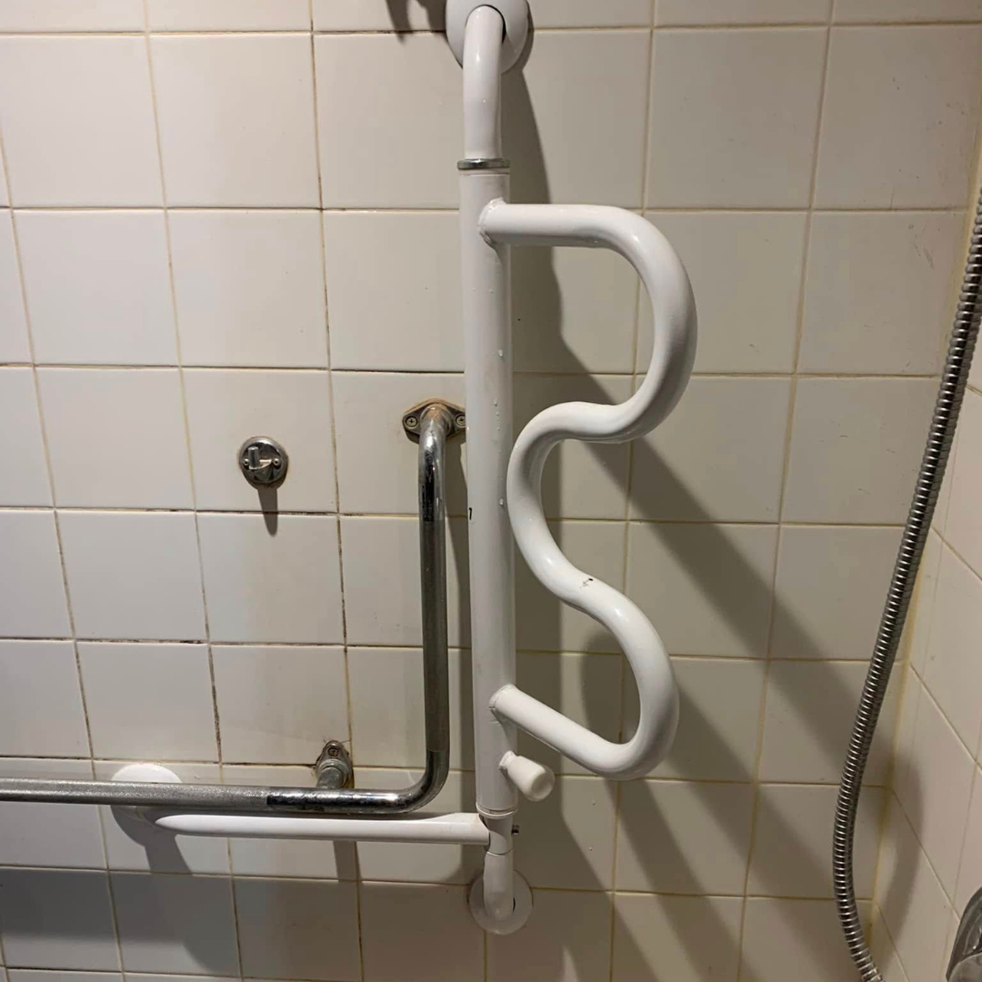 A Stander Curved Grab Bar in a shower with white tiled walls.