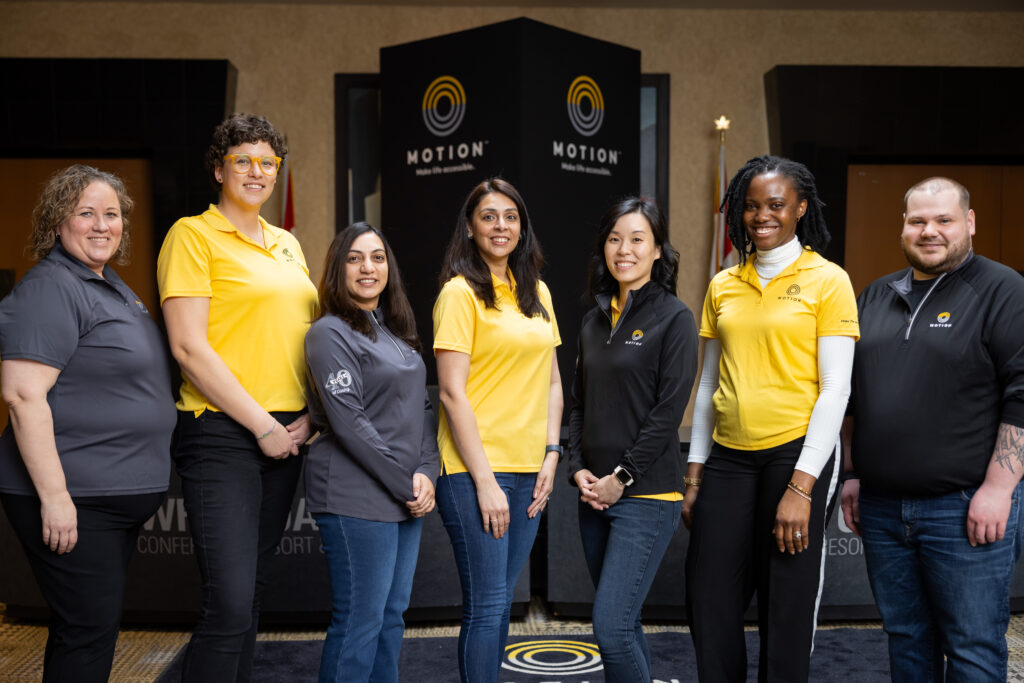 Seven members of Motion's HR team wearing Motion-branded uniforms and standing in front of a Motion-branded tower. 