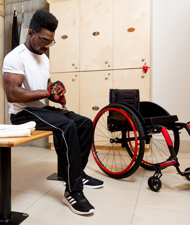 A young man putting on boxing gloves with his APEX C wheelchair beside him.